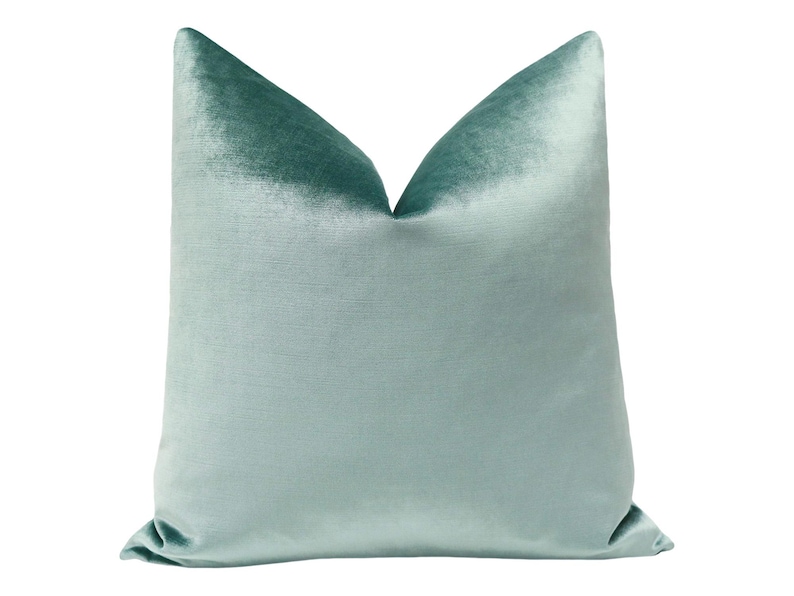 May include: A soft, light blue velvet pillow with a subtle sheen. The pillow is square and has a simple, elegant design.