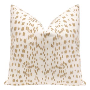 May include: A white pillow with a gold geometric pattern. The pattern is made up of small, irregular shapes that are scattered across the pillow.