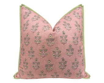 May include: A square decorative pillow with a pink floral pattern and a green border. The pillow features a repeating design of stylized floral sprigs in shades of green and white on a pink background.