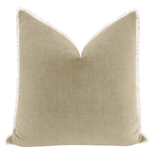 May include: A square, sage green pillow with a textured appearance. The pillow has a white fringe trim around the edges. The pillow is a decorative item for a bed or sofa.