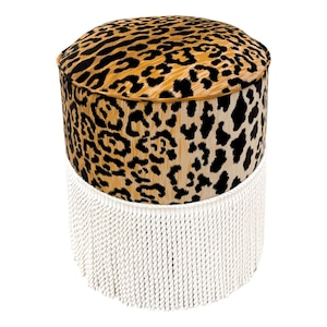 May include: A round, brown and black leopard print ottoman with a white fringe trim.