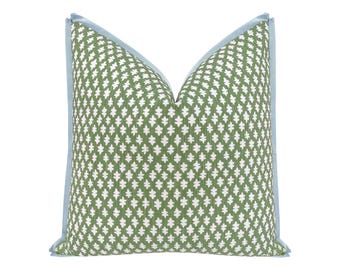 May include: A square throw pillow featuring a green fabric base with a repeating white leaf-like pattern. The pillow is finished with a light blue piping trim along all four edges, creating a distinct border around the patterned green surface.