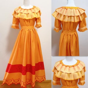 Puede incluir: Un vestido largo de color naranja con ribete rojo y blanco. El vestido tiene un cuello con volantes y mangas cortas.