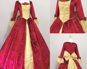 May include: A red velvet ball gown with a gold satin bodice and a rose detail. The gown has long sleeves and a full skirt.