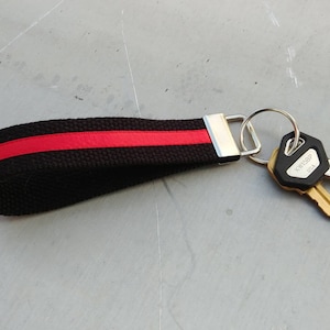 May include: Black and red key chain with a silver key ring and two keys. One key has a black plastic head with the text "KMF1589P" and "U.S.A.".