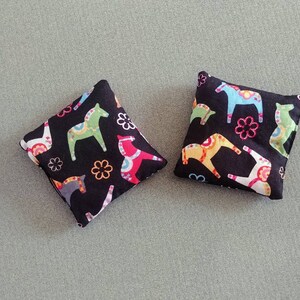 Puede incluir: Dos almohadas cuadradas de tela negra con un estampado de caballos Dala escandinavos de colores.