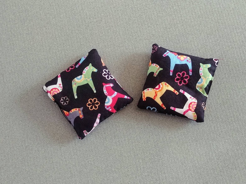 Puede incluir: Dos almohadas cuadradas de tela negra con un estampado de caballos Dala escandinavos de colores.