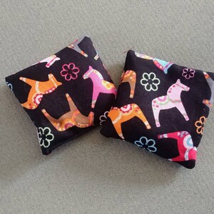 Puede incluir: Dos cuadrados de tela negra con un patr&oacute;n de caballos Dala coloridos y flores. Los cuadrados est&aacute;n cosidos juntos para crear una almohada.