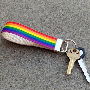 May include: A rainbow-colored key chain with a white background and a silver key ring. Two keys are attached to the ring, one is gold and the other is black.