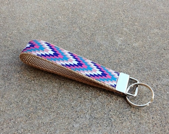 May include: A colorful key chain with a geometric pattern on a brown fabric strap and a silver key ring.