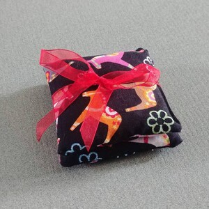 Puede incluir: Una bolsa de tela negra con una cinta roja atada alrededor. La bolsa est&aacute; decorada con un patr&oacute;n colorido de caballos y flores.