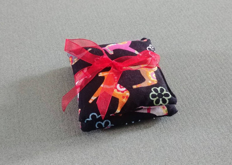 Puede incluir: Una bolsa de tela negra con una cinta roja atada alrededor. La bolsa est&aacute; decorada con un patr&oacute;n colorido de caballos y flores.