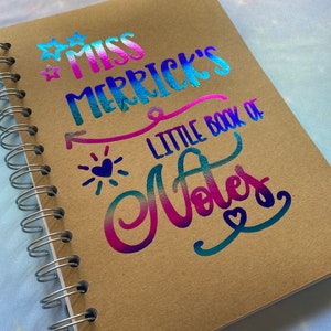 May include: A brown spiral bound notebook with a holographic rainbow design that says "Miss Merrick's Little Book of Notes" with stars and hearts.