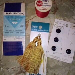 May include: Assortment of sewing supplies including a spool of red thread, navy blue seam binding, gold tassels, and black buttons. The seam binding is labeled "Wrights" and the thread is "Murphy's".