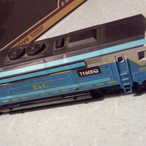 May include: A model train locomotive in blue, gray, and black. The train has the number 6610 and the text "T160EQ" printed on the side. The model is a detailed replica of a real train.