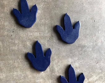 May include: Four dark blue dinosaur footprints made of wood. The footprints are arranged in a loose pattern on a gray concrete surface.