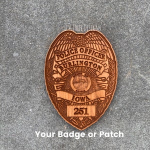 May include: A wooden police badge with the text "Police Officer Burlington State of Iowa 251" and the text "D+Three Designs" at the top.