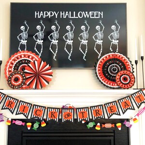 May include: A black and white banner with the words "Trick or Treat" in orange letters. The banner is decorated with black and white stripes and is hanging above a fireplace. There are red, orange, and yellow candy decorations hanging from the banner.