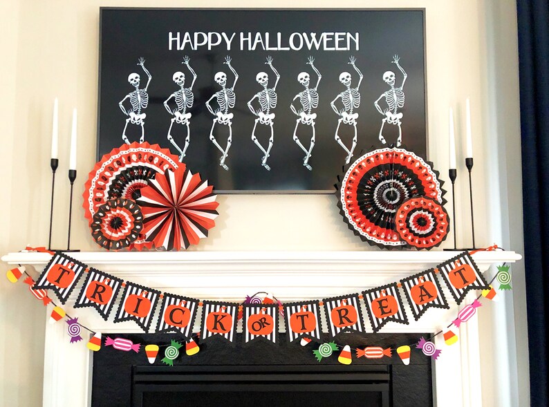 May include: A black and white banner with the words "Trick or Treat" in orange letters. The banner is decorated with black and white stripes and is hanging above a fireplace. There are red, orange, and yellow candy decorations hanging from the banner.
