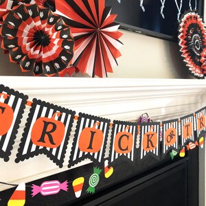May include: Black and white striped banner with the words "Trick or Treat" in orange and black letters. The banner is decorated with orange and black pumpkin cutouts and colorful candy cutouts.