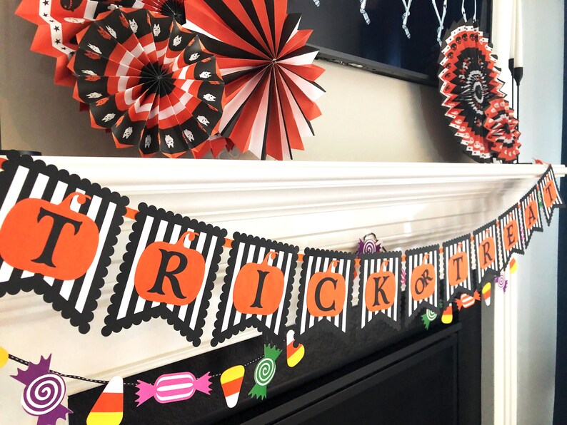 May include: Black and white striped banner with the words "Trick or Treat" in orange and black letters. The banner is decorated with orange and black pumpkin cutouts and colorful candy cutouts.