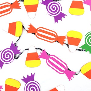 May include: A Halloween garland with paper cutouts of candy corn, lollipops, and wrapped candies in orange, yellow, green, pink, and purple.