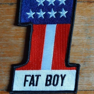 May include: A black and white embroidered patch with a red, white, and blue American flag design in the shape of the number one. The patch has the text "FAT BOY" in black lettering on a white background.