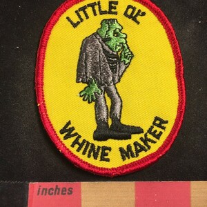 Pode incluir: Um remendo bordado amarelo com um monstro de desenho animado e o texto "Little Old Wine Maker".