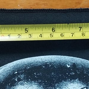 May include: Black rectangular patch with a white graphic design. A yellow tape measure shows the patch is approximately 10 inches long. The patch is on a wooden surface.