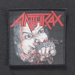 May include: Square black patch featuring the band name "ANTHRAX" in red, above a detailed illustration of a person clenching a chain in their fist. The image is in red, white, and black. The text "©2020 ANTHRAX" is at the bottom.