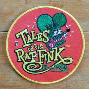 May include: A red, yellow and green embroidered patch with the text "Tales of the Rat Fink Ed "Big" Roth" and a cartoon image of a green monster with a toothy grin.