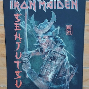 Op de afbeelding: Zwart rechthoekig embleem met de bandnaam "IRON MAIDEN" in een gestileerd lettertype. De afbeelding toont een samoerai-krijger met een zwaard, met Japanse tekst aan de linkerkant. De krijger is in tinten rood, bruin en blauw.
