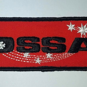 May include: Red embroidered patch with black lettering that reads "OSSA" and white stars. The patch has a black border.