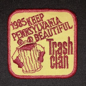 May include: A yellow and red embroidered patch with the text "1985 Keep Pennsylvania Beautiful Trash Can". The patch features a cartoon trash can with arms and legs.