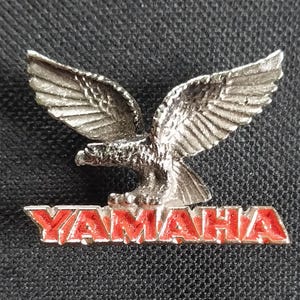 May include: A silver eagle with outstretched wings and the word "YAMAHA" in red letters below.