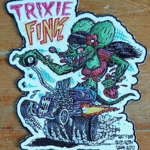 May include: A green, cartoon rat with a pink flower in her hair, driving a purple hot rod with flames coming out of the exhaust. The rat is wearing a red and white top and a black headband. The text "TRIXIE FINK" is above the rat and the text "RAT FINK © ED ROTH 1954-2012" is below the rat.