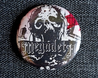 May include: A round button with a black and white skull graphic and the word "Megadeth" in a banner. The button has a red and white background and is set against a dark blue textured surface.