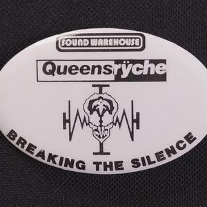 May include: White oval button with black text and graphics. The button features the text "SOUND WAREHOUSE" at the top, the band name "Queensrÿche" in the center, and the phrase "BREAKING THE SILENCE" at the bottom. A graphic of a skull and sound waves is in the center.