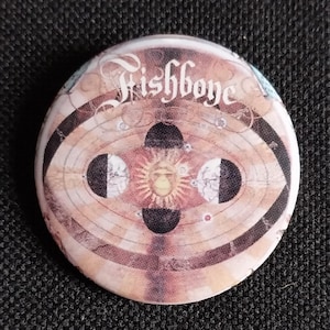 May include: A round button with a brown and white design featuring the text "Fishboy" in a stylized font. The design includes a sun and three moons.