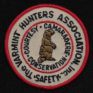 May include: A white and red embroidered patch with the text "The 'Safety First'  Hunters Association - Courtesy - Camaraderie - Conservation" and a brown gopher standing on its hind legs.