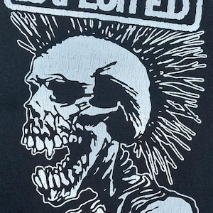 Könnte beinhalten: Schwarze Grafik mit einem Totenkopf mit Irokesenschnitt und dem Bandnamen "THE EXPLOITED" in Weiß. Der Totenkopf hat einen geöffneten Mund und spitze Zähne. Text: "© 2016 The Exploited. U.L.T. Razamataz. Made in England."