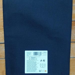 May include: A dark navy blue rectangular patch with a white label in the upper right corner. The label contains text, a barcode, and various symbols. The patch is lying on a wooden surface.