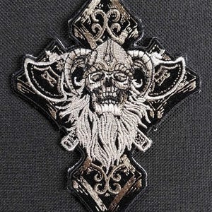 Könnte beinhalten: Ein gestickter schwarzer und silberner Aufnäher mit einem Schädel mit Hörnern und Bart, umgeben von einem Kreuzdesign. Der Schädel trägt einen Helm mit einem einzigen Auge.