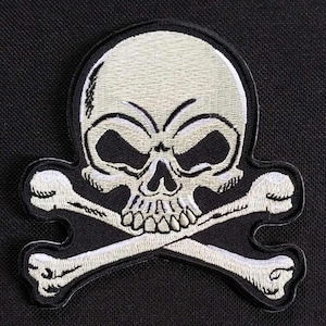 Könnte beinhalten: Weiß gestickter Totenkopf- und Knochen-Patch. Der Totenkopf hat ein detailliertes Design mit einer gerunzelten Stirn und einem bedrohlichen Ausdruck. Die Knochen sind einfach und symmetrisch.