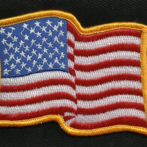 May include: A red, white, and blue embroidered American flag patch with a yellow border. The flag is waving in the wind.