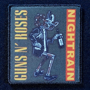 Puede incluir: Parche rectangular con una ilustración de esqueleto sosteniendo una botella. El parche presenta las palabras "GUNS N' ROSES" y "NIGHTRAIN" en naranja. El fondo es gris oscuro con un borde negro.
