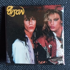 May include: A vintage button featuring a black and white photo of two people. The band's name "Poison" is written in yellow letters on the top left corner of the button.
