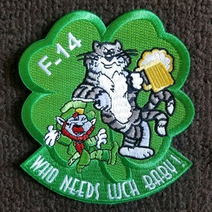 Puede incluir: Un parche verde en forma de trébol con un gato de dibujos animados sosteniendo una jarra de cerveza y un duende. El parche tiene el texto "F-14" y "Who Needs Luck Baby!" en blanco.