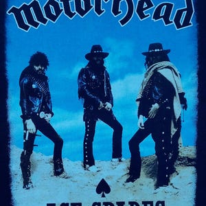 May include: Black t-shirt featuring the band Motörhead with the text "Motörhead" in a stylized font above three figures. Below the figures is the text "ACE OF SPADES" and a spade symbol.