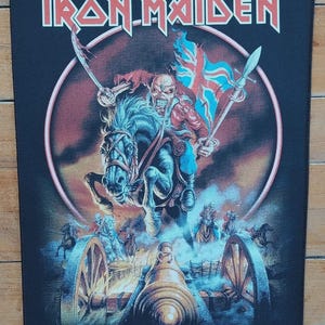 May include: Black patch featuring the band name "IRON MAIDEN" in red and white lettering. The image depicts a skeletal figure on horseback, holding a sword and a flag with a Union Jack design, with a cannon in the foreground.